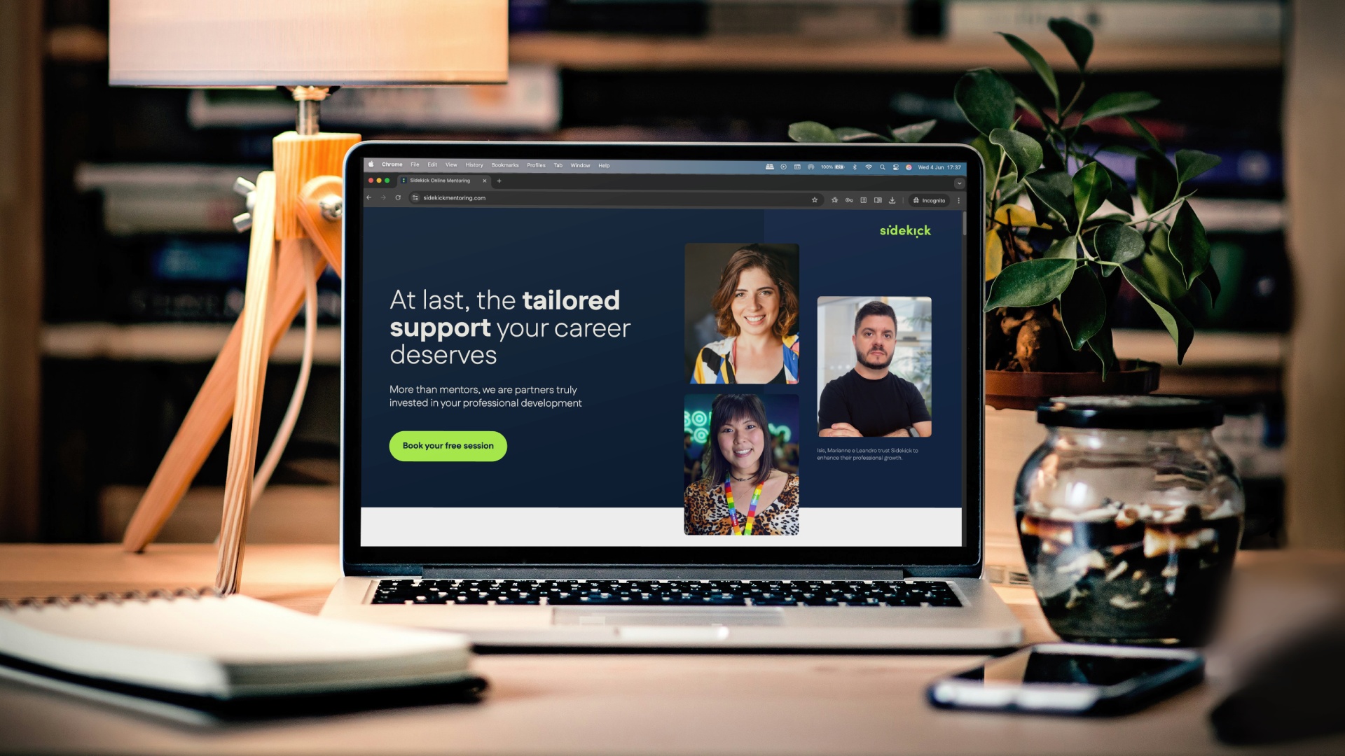 A macbook on a table. Cozy environment. The screen shows Sidekick Mentoring's website.